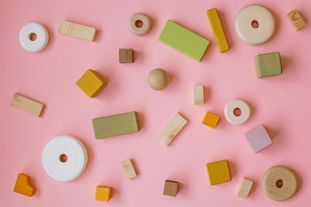 Flatlay of various wooden shapes on a pastel pink background, perfect for creative and playful designs.